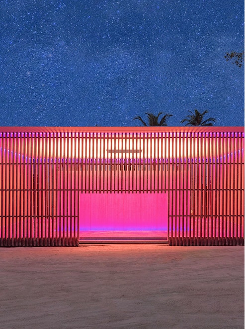 Silhouette of a person standing before a warmly lit architectural facade.